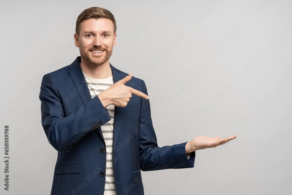 Smiling happy business man pointing index finger on hand on copy space isolated on studio gray background. Banner for advertisement, marketing, sales, offer discount. Promotional concept of low prices Smiling happy business man pointing index finger on hand on copy space isolated on studio gray background. Banner for advertisement, marketing, sales, offer discount. Promotional concept of low prices