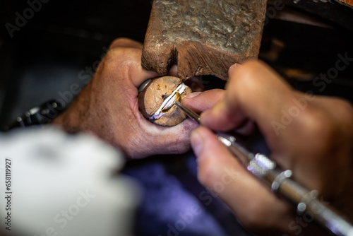 Jeweler hands setting a diamond into a ring with a burin in a jewelry workshop. Goldsmith working and creating a gold jewel. photo