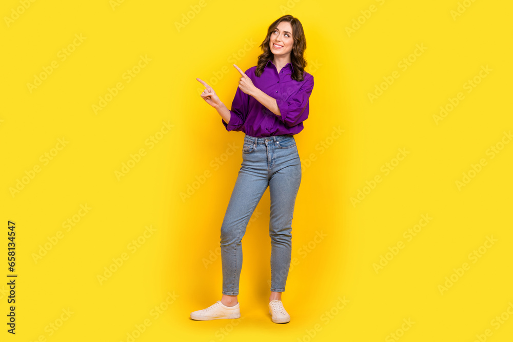 Full size portrait of nice cheerful girl look indicate fingers empty space isolated on yellow color background Full size portrait of nice cheerful girl look indicate fingers empty space isolated on yellow color background