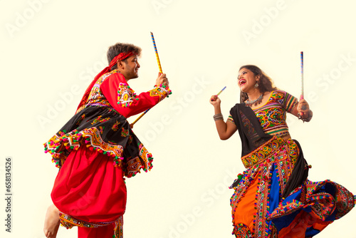 A  happy young couple performing Dandiya Raas on a black background, during Navratri celebrations