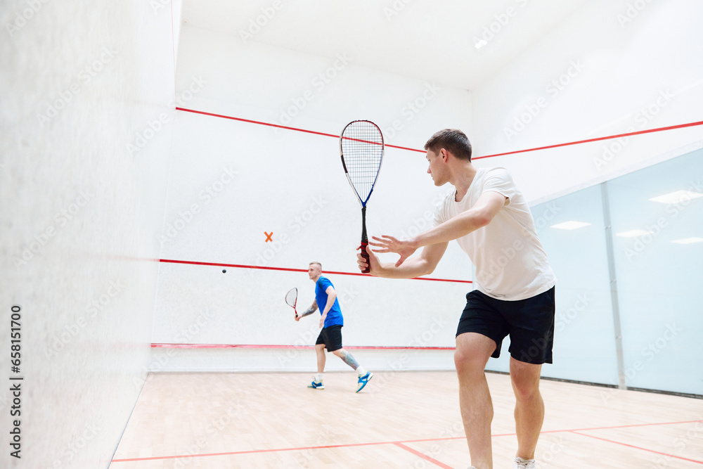 Two young, concentrated and sportive men, friends playing squash together on squash court. Exercising and leisure. Concept of sport, hobby, healthy and active lifestyle, game, gym, ad