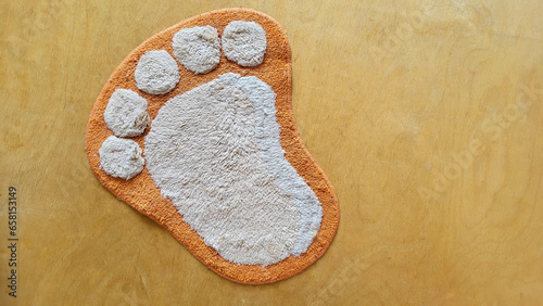 Funny fluffy rug in the shape of a foot on a beige wooden floor.