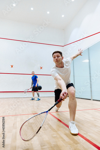 Young concentrated, athletic man playing squash, training on squash court, hitting ball with racket. Concept of sport, hobby, healthy and active lifestyle, game, gym, ad