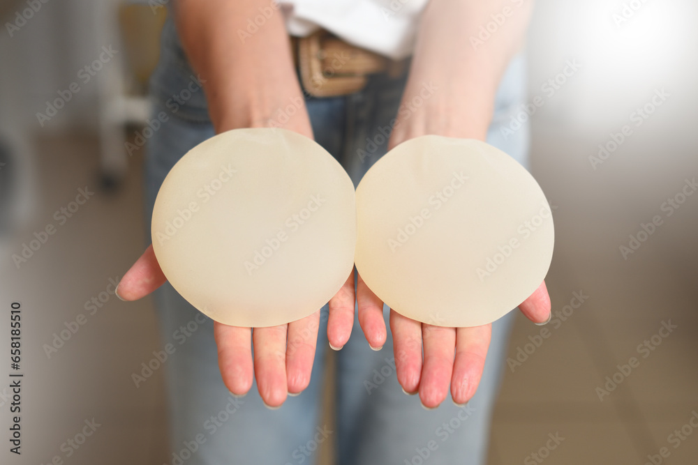 Woman showing breast augmentation implants in her hands - obrazy, fototapety, plakaty 