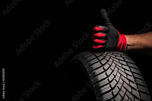 Car tire service and hands of mechanic holding new tyre on black background with copy space for text © ValentinValkov