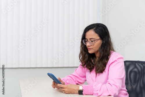 Portrait of a psychopedagogue, wearing pink clothes, in her office, sitting, looking at the appointments scheduled on her cell phone. Helps with school performance.