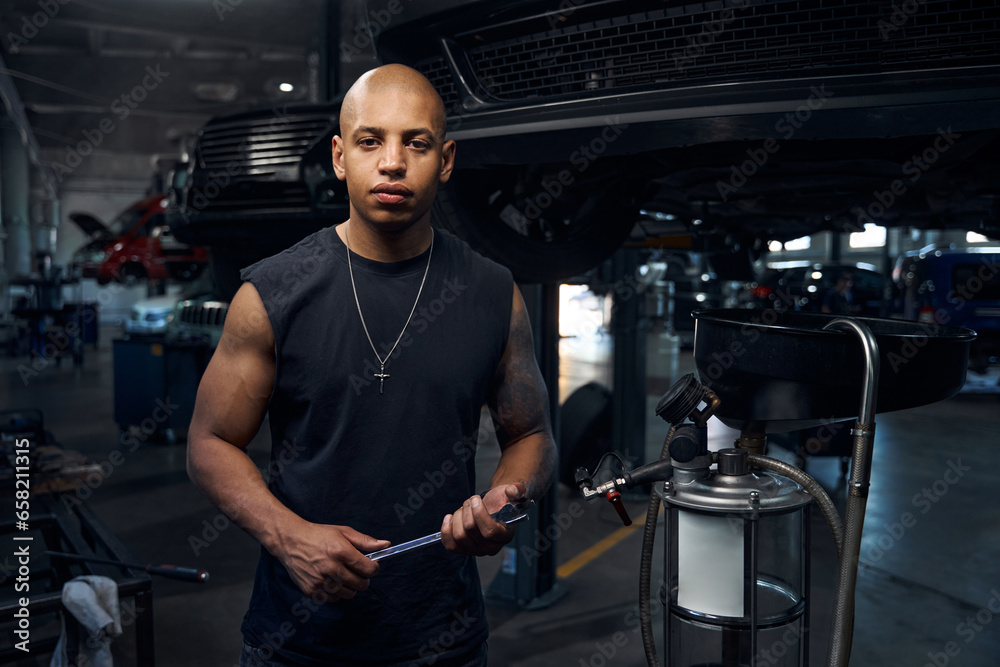 Bulking auto-mechanic holding many wrenches in hands looking at camera