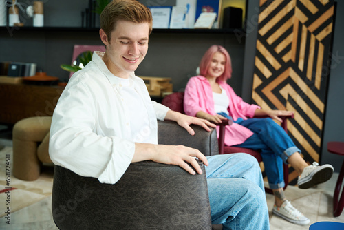Smiling guy and woman are sitting in comfortable armchairs