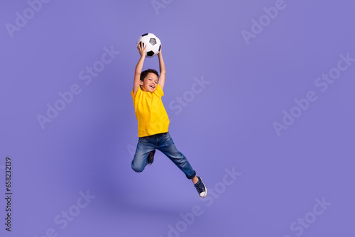 Full size photo of cute young schoolboy jumping catch football ball wear yellow clothes isolated on purple color background