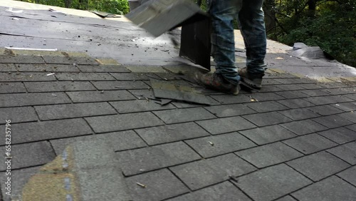 Closeup view of roofer removing old roof shingles to be replaced with new roof in house renovation project