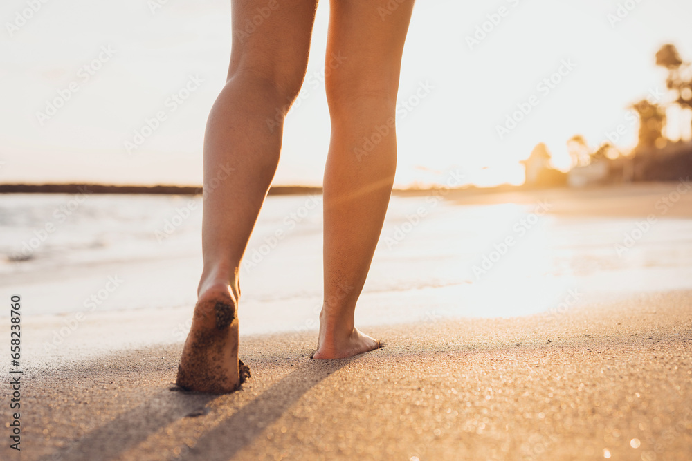 Beach travel - woman walking on sand beach leaving footprints in the sand. Closeup detail of female feet and golden sand on Tenerife beach.
 - obrazy, fototapety, plakaty 