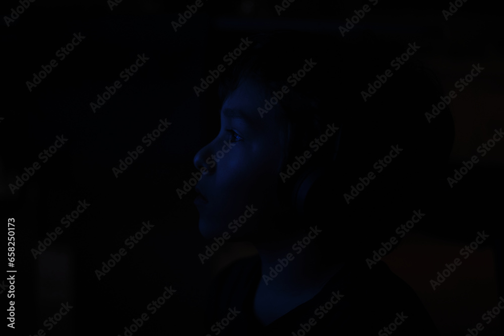 silhouette of a frightened boy who sits on the floor in a depressive phase, in a dark room