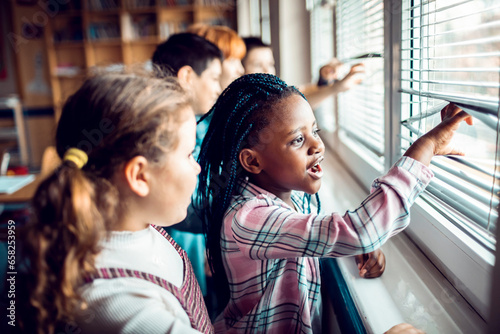 Young and diverse pupils looking out the window in a elementary school classroom photo