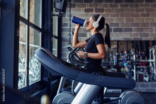 Female athlete during water break on a treadmill in a gym.