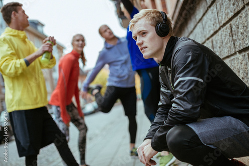 Young man listening to music on his headphones while getting ready to run with his friends in the city