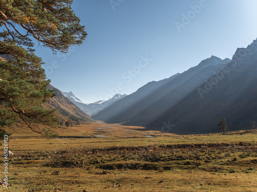 The path in the mountains at the sunset with deep shades, sun rays and snowtops in a distance photo