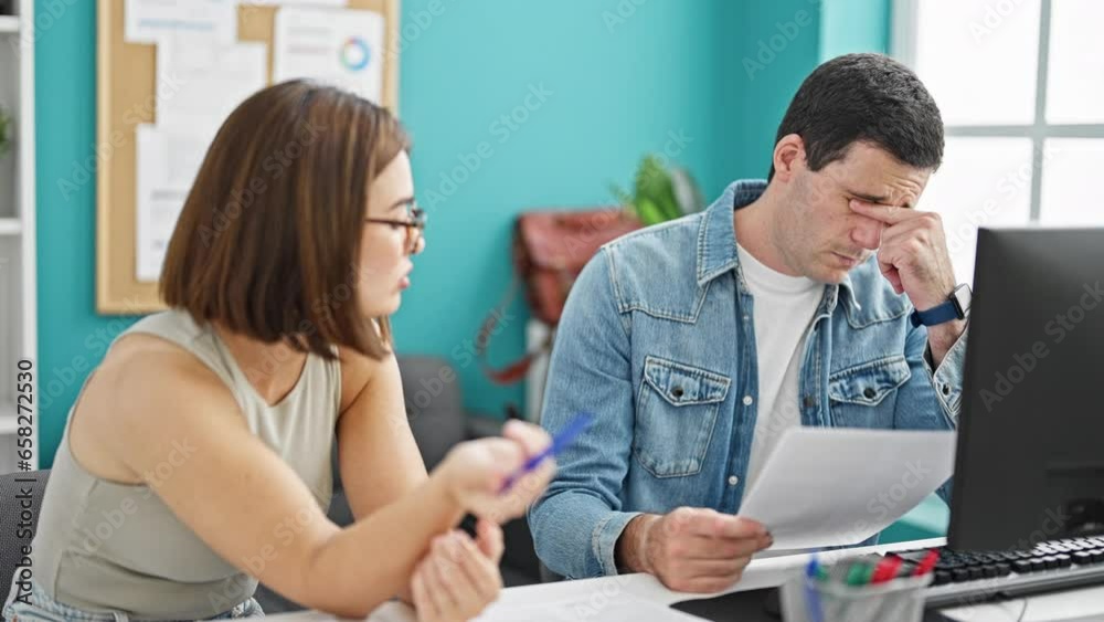 Two workers man and woman sitting on table reading document looking upset at the office Two workers man and woman sitting on table reading document looking upset at the office