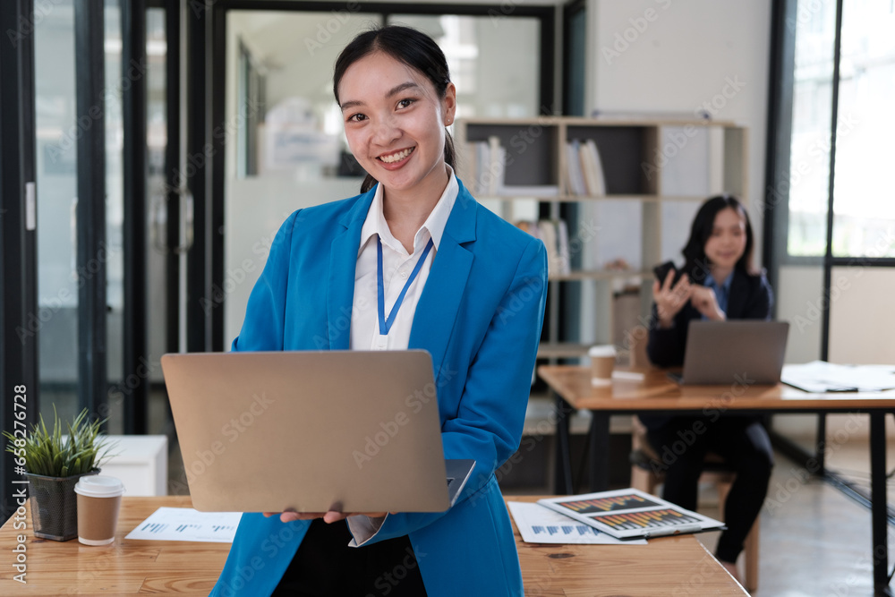 Charming Asian woman working at the office using a laptop Looking at the camera. Charming Asian woman working at the office using a laptop Looking at the camera.