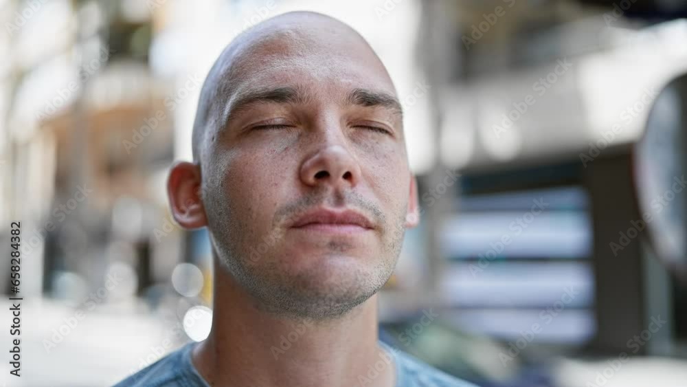 Young hispanic man standing with serious expression and closed eyes at street