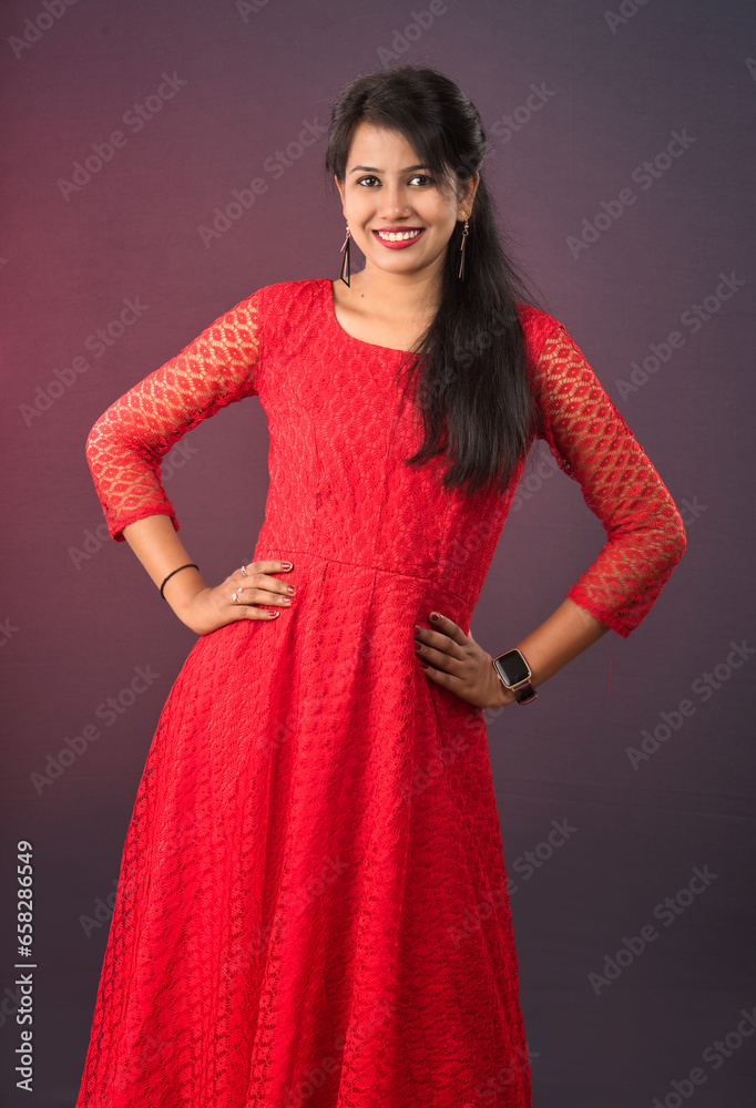 Portrait of a beautiful, smiling, young Indian girl wearing a red dress posing on a dark background