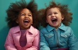 Two joyful toddlers laughing heartily against a turquoise backdrop.