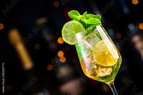 Hugo spritz cocktail drink with sparkling wine, elderflower syrup, soda, lime, mint and ice, dark bar counter background, close-up