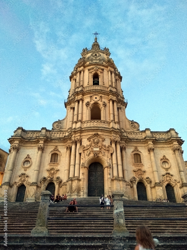 The majestic facade of the San Giorgio Cathedral in Modica stands tall against the sky. This Sicilian Baroque masterpiece captivates with its rich ornamentation and architectural grandeur.