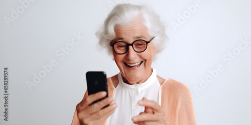 A beautiful elderly woman in glasses on a white background looks at the phone and smiles