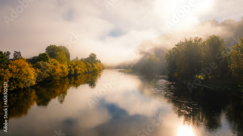 Early morning mist over the Dordogne river in France surrounded by autumnal trees