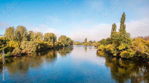 Early morning sunlight on the Dordogne river in France surrounded by autumnal trees along the banks of the river