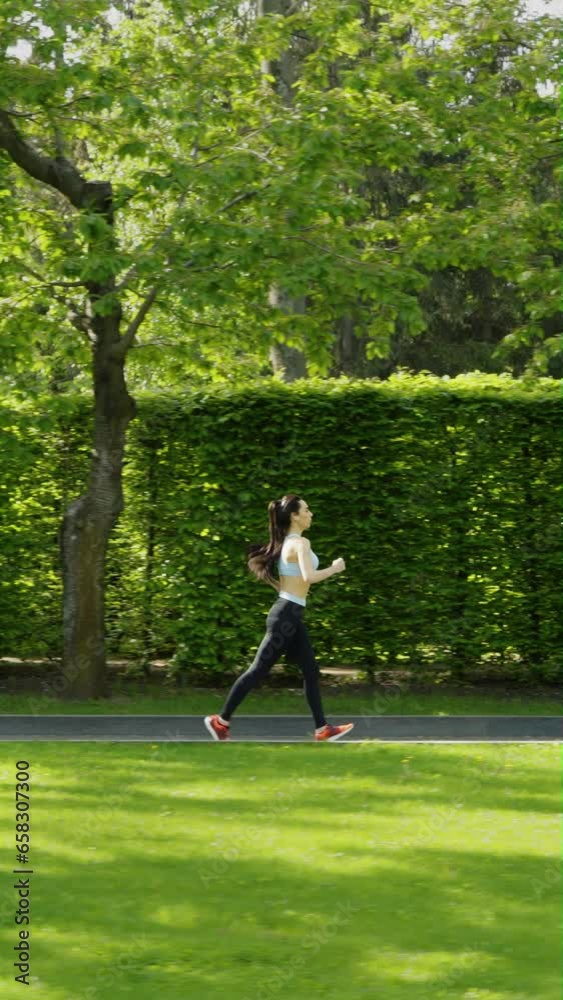 Vertical Screen: Slow motion fit woman in sportswear jogging against garden maze on summer morning. Tracking shot of female athlete exercising outside. Healthy lifestyle. Concept of fitness Vertical Screen: Slow motion fit woman in sportswear jogging against garden maze on summer morning. Tracking shot of female athlete exercising outside. Healthy lifestyle. Concept of fitness