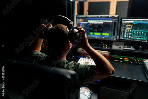 a male sound engineer sits at a mixing desk with his back to camera and puts on headphones