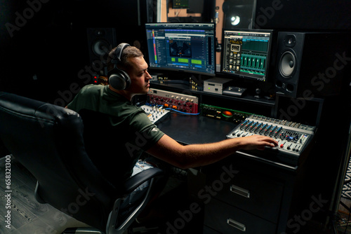 a focused male sound engineer wearing headphones sits at a mixing desk recording new track