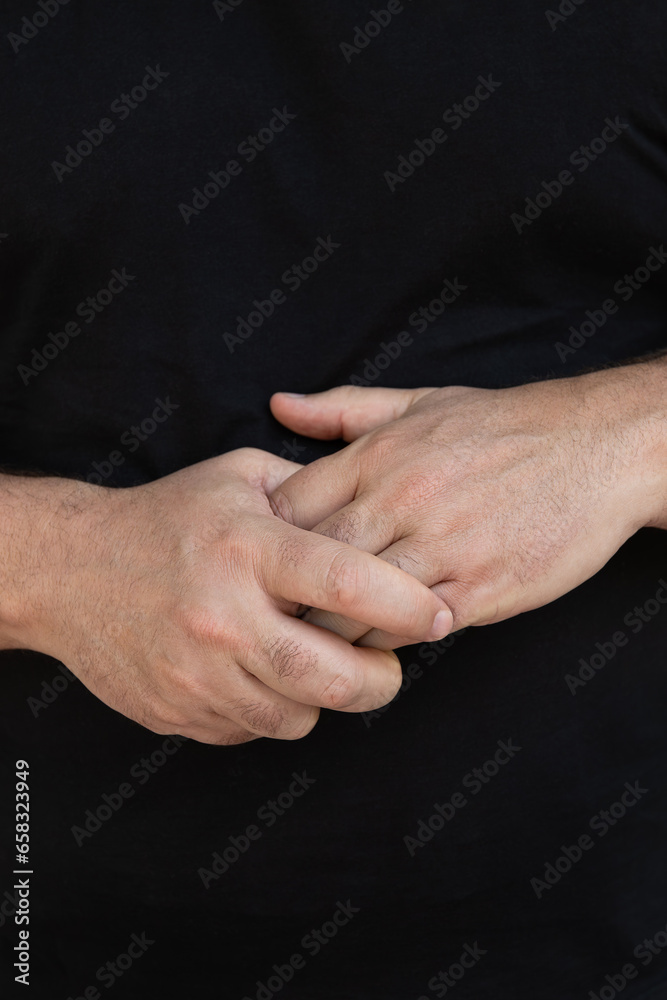 Close-up detail of the hands of a man in his 50's intertwined on a black background. Natural light