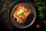 Traditional homemade lasagna with minced meat, bolognese sauce topped with cheese and basil leafs served on a plate on the dark rustic table, top view