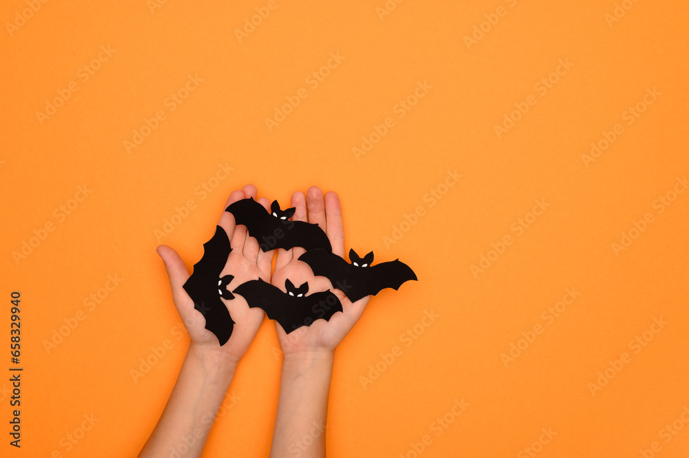 Halloween decorations black bats in the hands of a child on an orange background. Halloween concept. Halloween card Halloween decorations black bats in the hands of a child on an orange background. Halloween concept. Halloween card