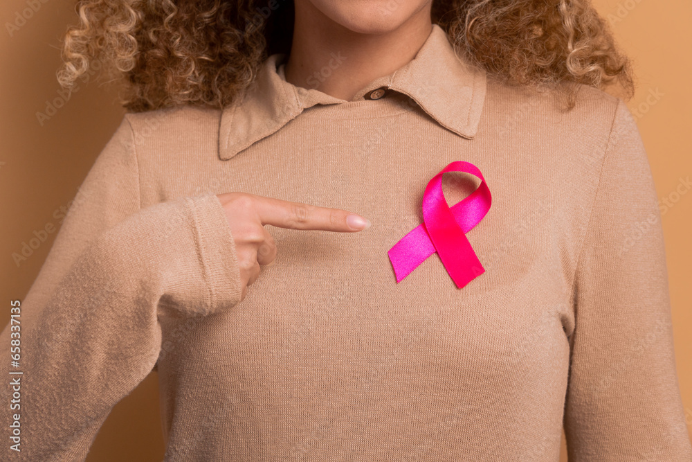hands of teen girl showing pink ribbon in beige studio background. breast cancer, awareness concept. hands of teen girl showing pink ribbon in beige studio background. breast cancer, awareness concept.