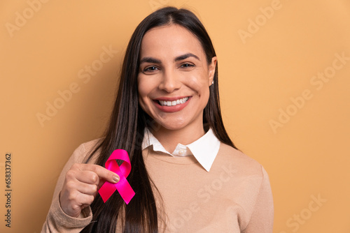 happy young woman showing pink ribbon in beige background. breast cancer, awareness concept. photo