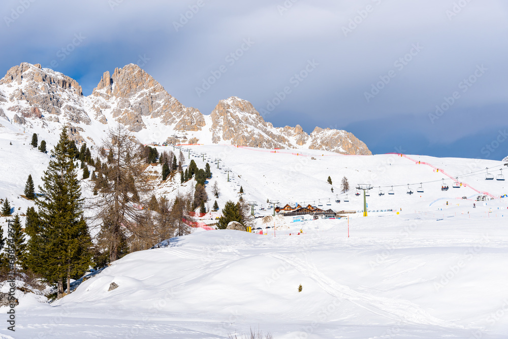 Chairlifts and ski slopes at the foot of towering snow-capped rocky peaks in the dolomites on a sunny winter day