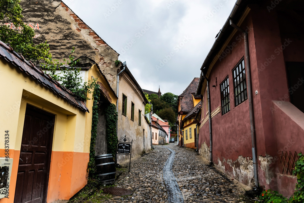 Old medieval street with colorful houses and in the background is the church on the hill. Sighisoara, Romania.