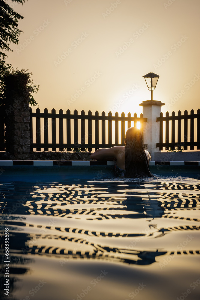 Backlit woman in the pool, at sunset. Scene that inspires tranquility