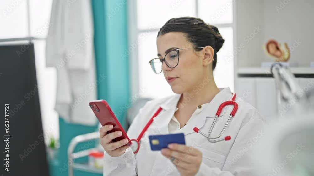Young beautiful hispanic woman doctor using smartphone working doing online shopping at the clinic Young beautiful hispanic woman doctor using smartphone working doing online shopping at the clinic