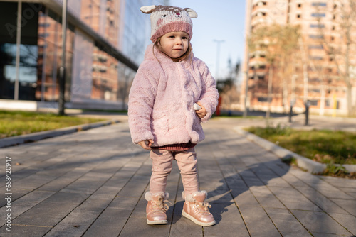 Small caucasian girl toddler stand in the city outdoor in winter day