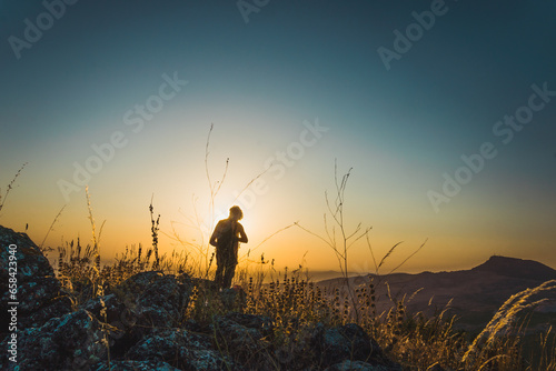 Silhouette of a young boy standing with the sun in the background of the scene at sunset in the hills in Subbetic Mountains in Cordoba, Spain