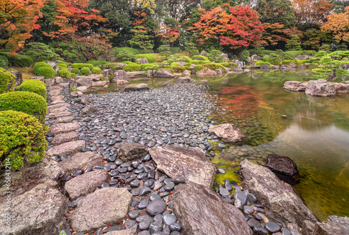fukuoka, kyushu - dec 07 2022: Natural autumn landscape depicting the pebbles shore wet by rain on the pond of the Japanese traditional garden of the Ohori garden with maple momiji trees surrounding. photo