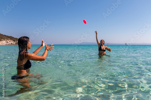 Beautiful young women playing frisbee on sea beach.Two young girls playing with a plastic disc in the water.Travel, vacation and fun