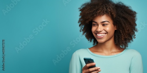 Horizontal shot of happy dark skinned Afro American woman enjoys mobile communication and modern technologies poses against blue background points away on free space for your advertisi : Generative AI