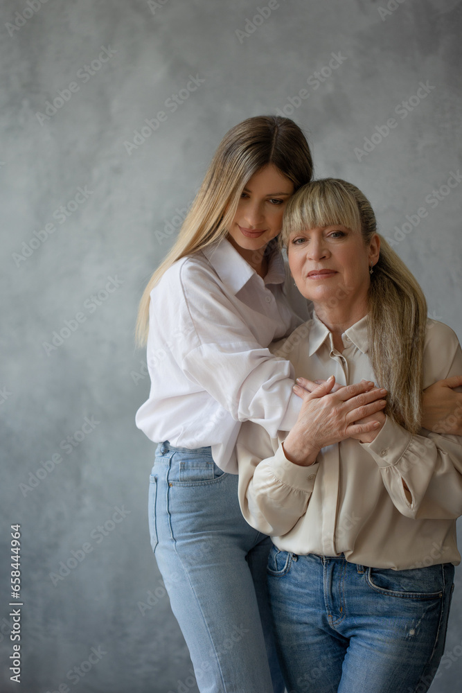 Happy family, women together. Mom and adult daughter smile at each other, studio photo in casual style Happy family, women together. Mom and adult daughter smile at each other, studio photo in casual style