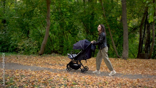 A young mother walks through the forest with a sleeping child in a stroller. A woman with glasses walks in an autumn park.