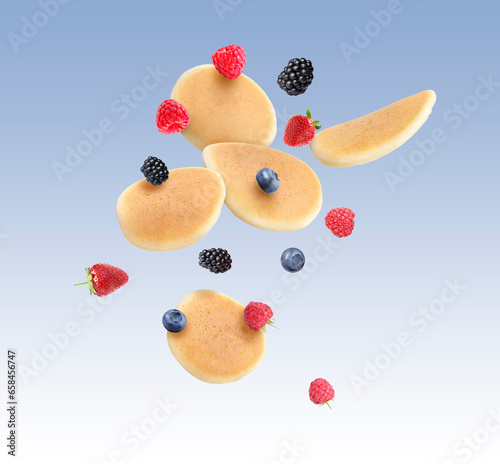 Many fresh pancakes and berries flying on pale blue background